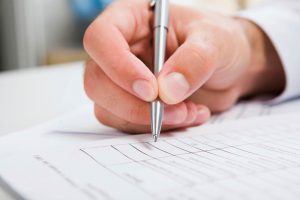 Male hand is writing in business document lying on the table